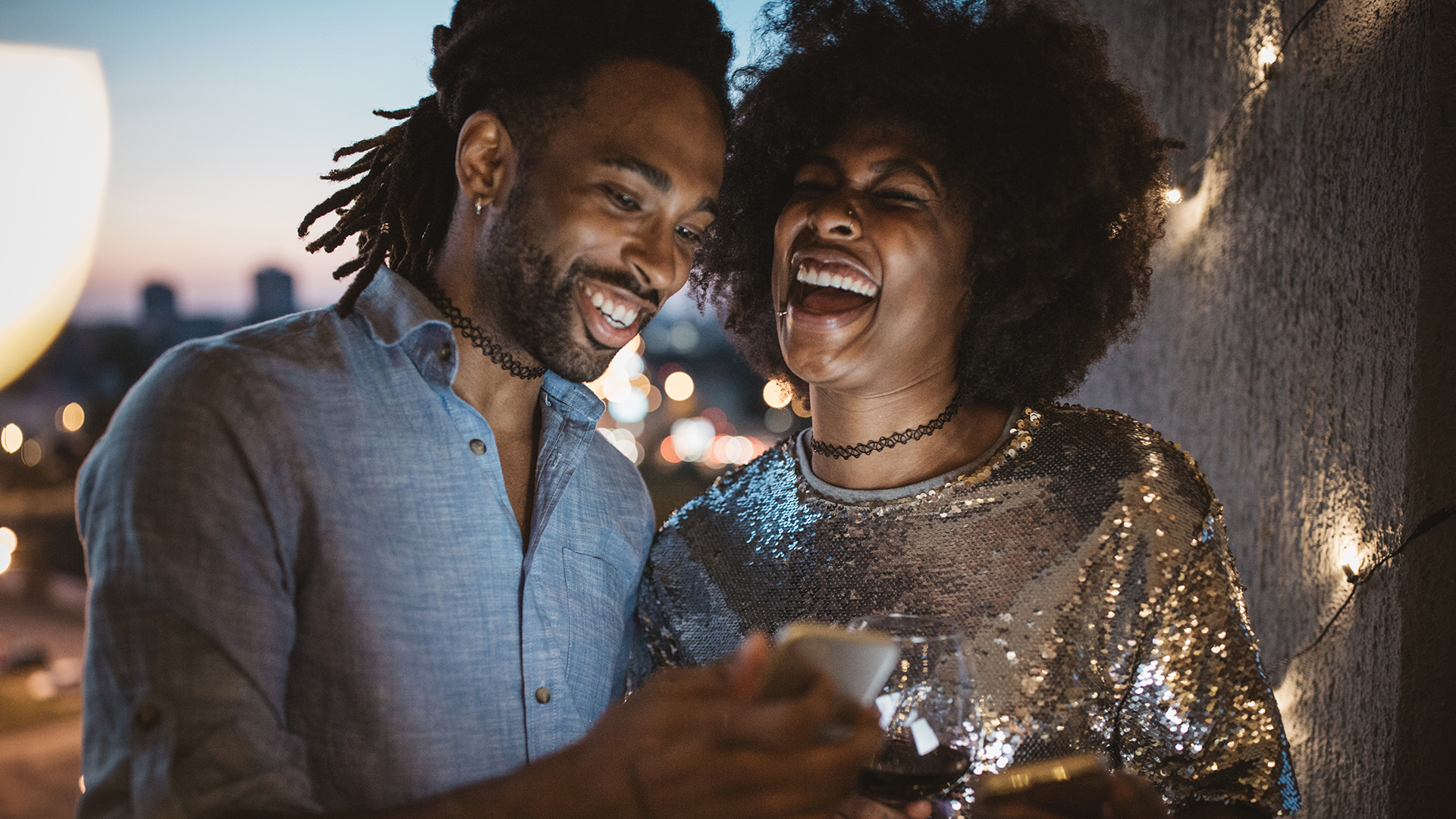 Man and woman laughing outside, looking at phone