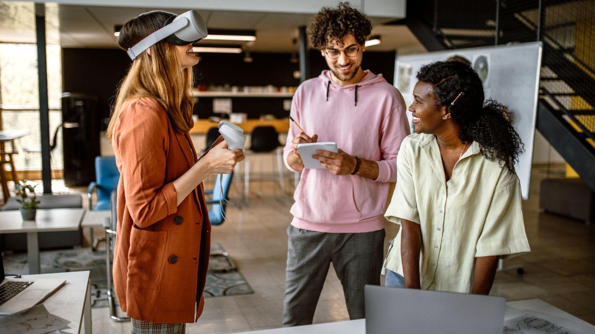 Three people in an office. One person wearing a VR headset.