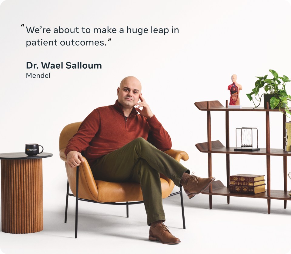 A picture of a man in a red sweater sitting on a modern-looking armchair.